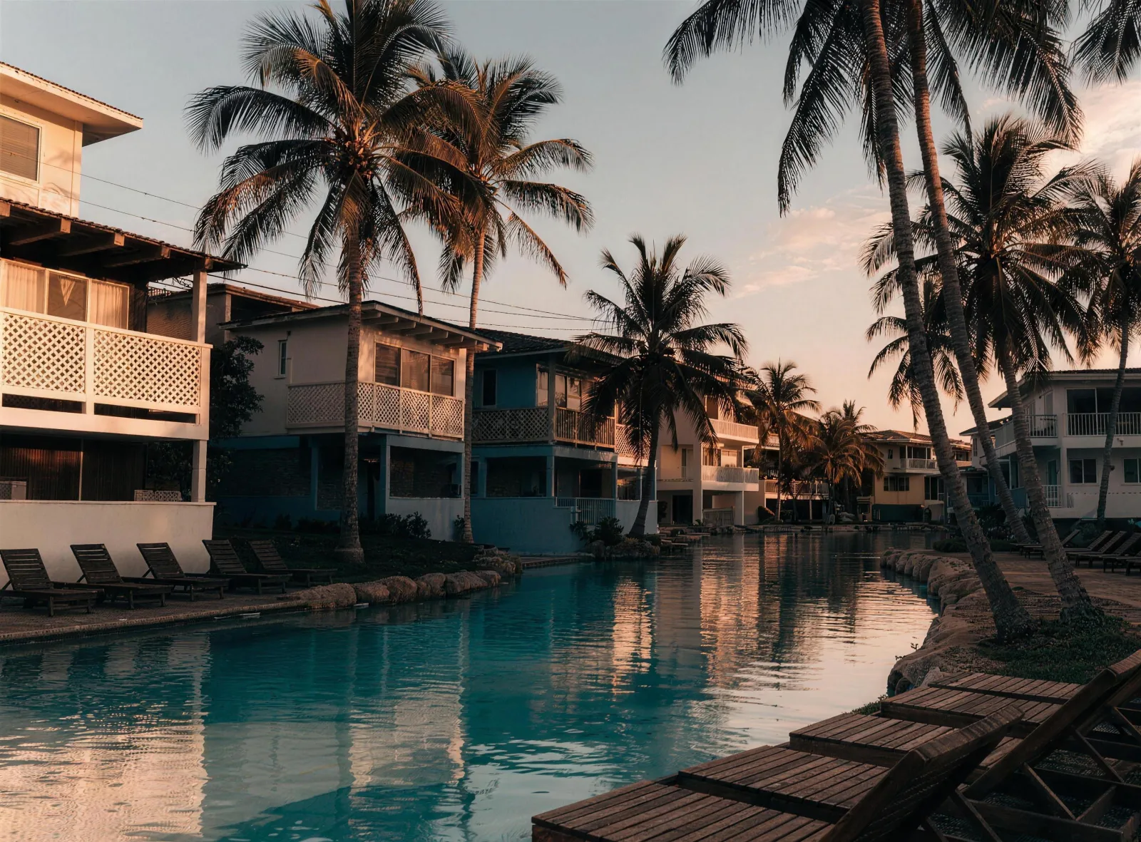 Lagoon-style pool at dusk ringed by palms and pastel houses, loungers empty